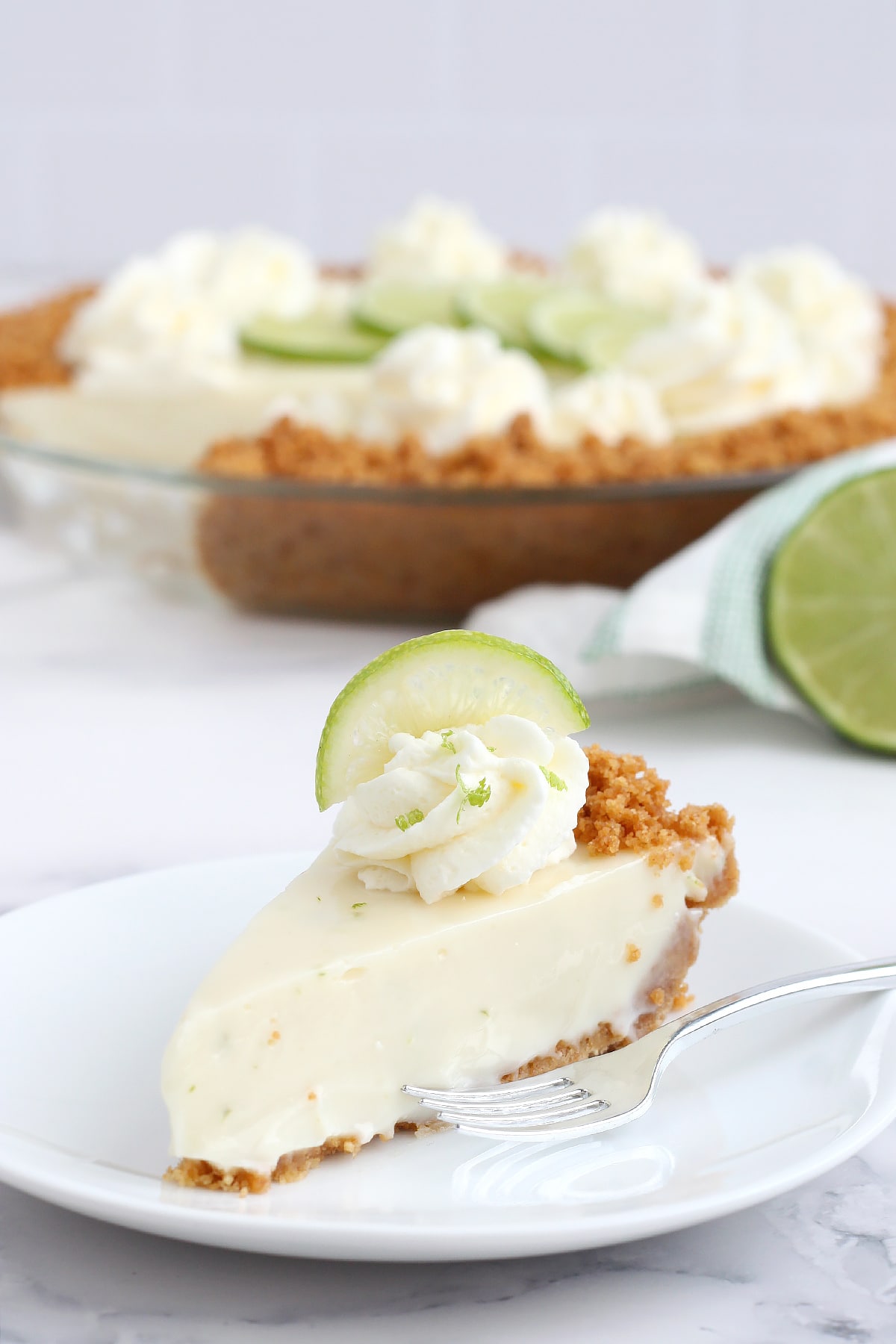 A slice of key lime pie on a white serving plate topped with a swirl of whipped cream and lime zest.