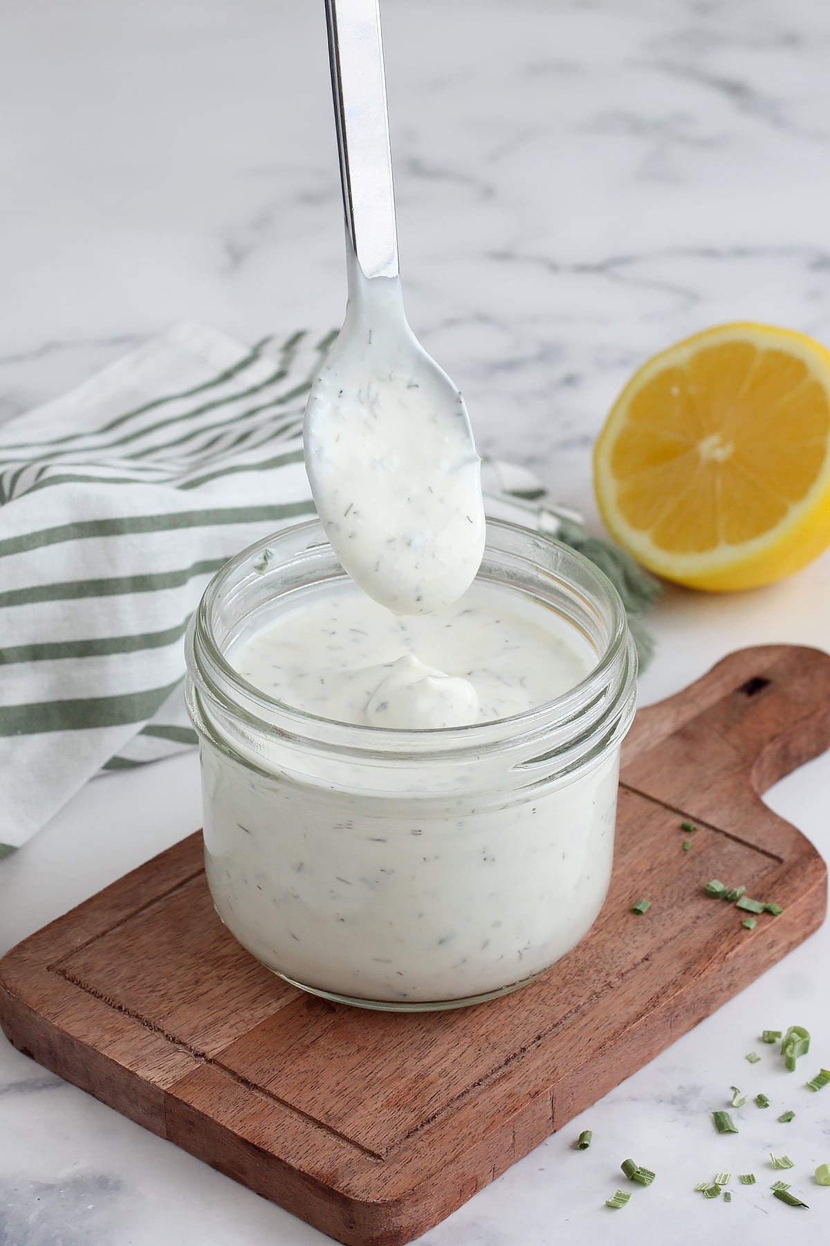 Ranch dressing in a jar, being scooped out with a spoon on a small wooden cutting board.