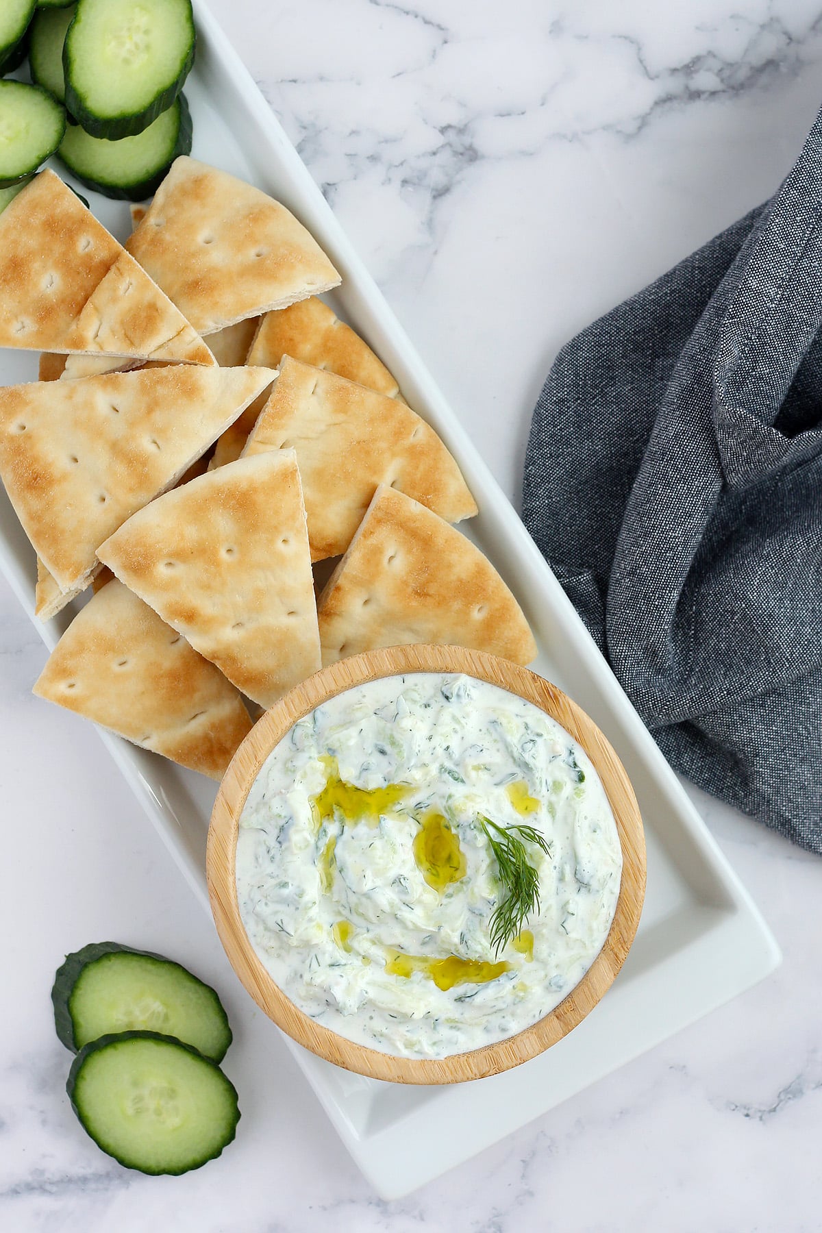 Homemade Tzatziki Dip drizzled with olive oil with fresh pita and a blue linen.