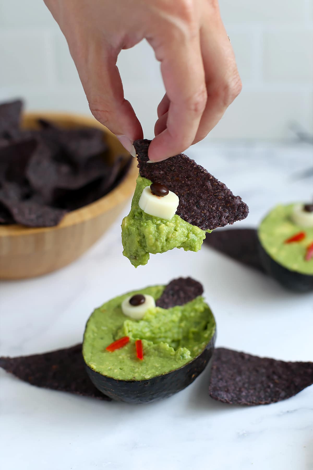 Someone scooping guacamole out of an avocado bowl with a blue corn chip.