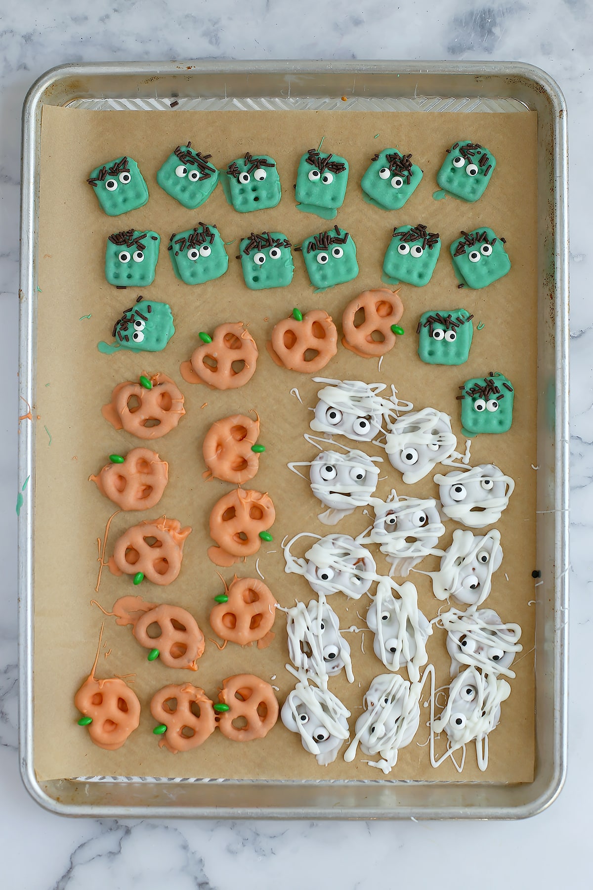 A baking sheet lined with brown parchment paper and topped with chocolate dipped halloween pretzels.