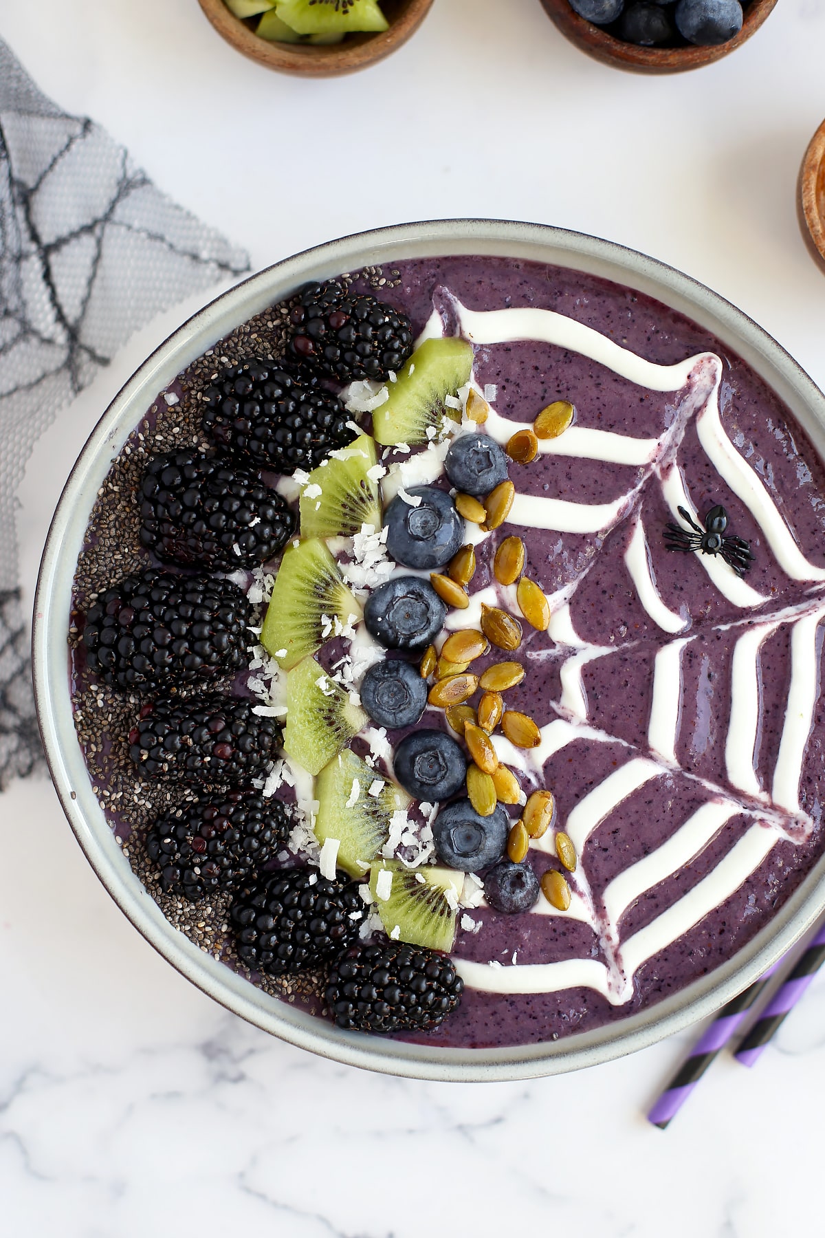 Halloween smoothie bowl topped with a web design, blackberries, chia seeds and kiwi slices.