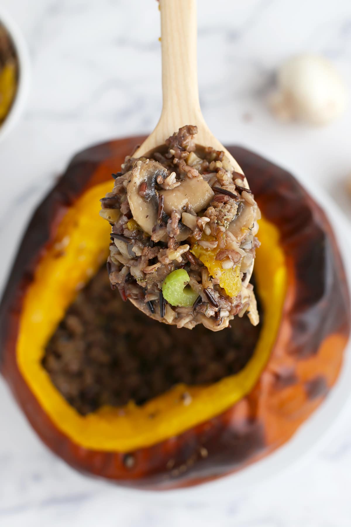 Baked pumpkin stuffed with rice, ground beef, mushrooms and celery scooped out with a wooden spoon.