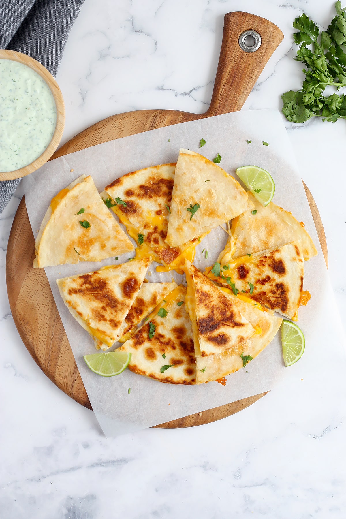An overhead shot of homemade cheese quesadillas on flour tortillas and topped with chopped cilantro and lime slices.