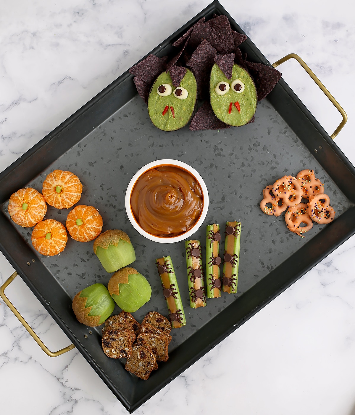 A black tray that is being set up with halloween snacks.