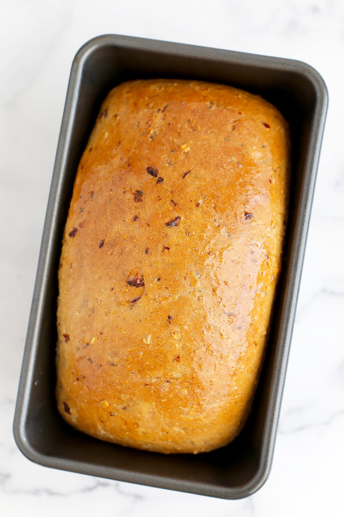 A loaf of golden brown cinnamon raisin bread in a metal loaf pan.