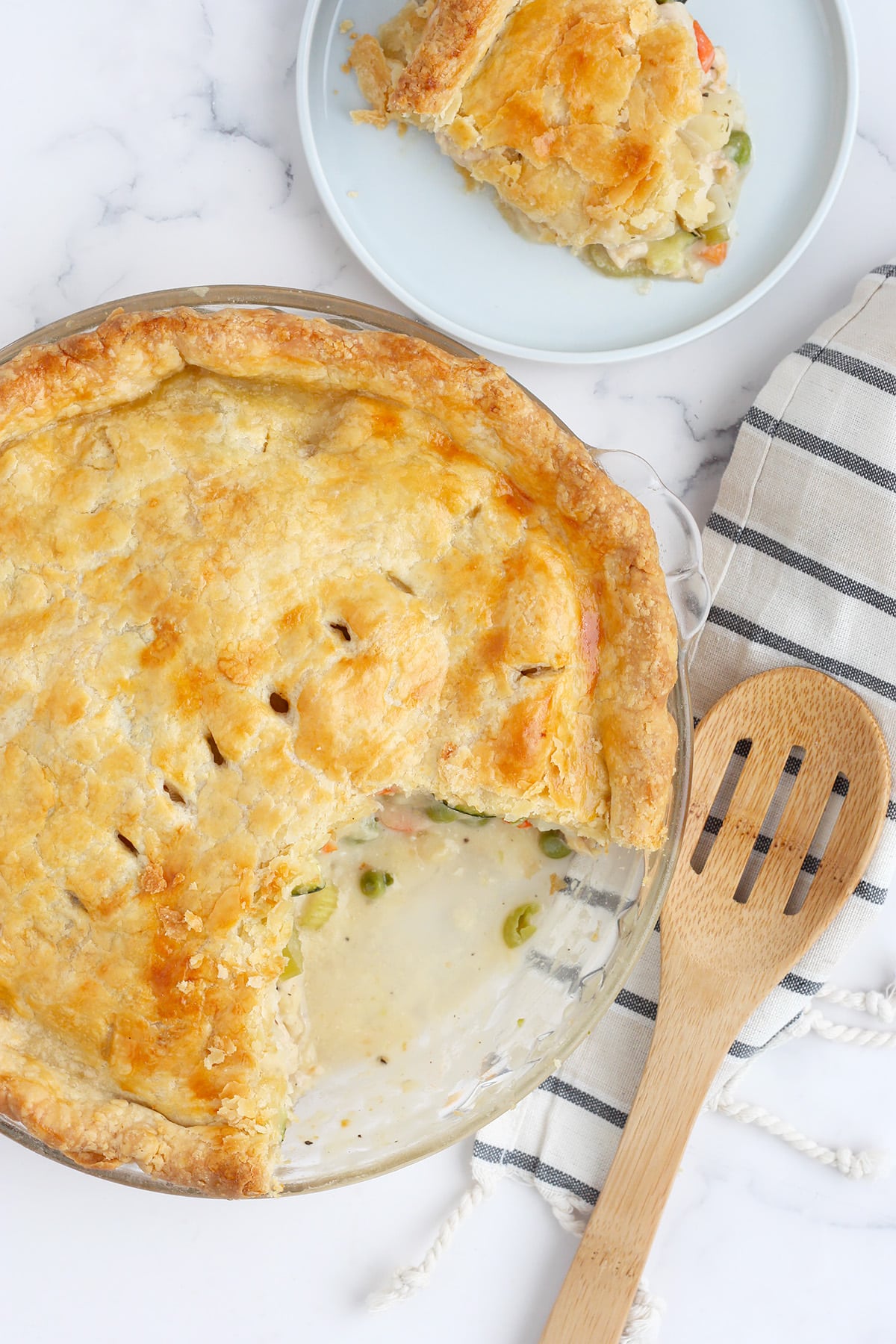 An overhead shot of homemade chicken pot pie in a glass pie dish with a wooden serving spoon.