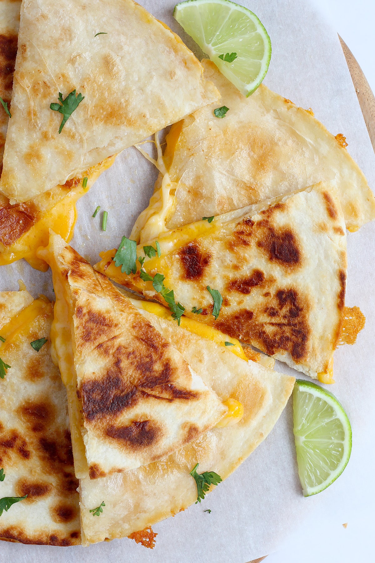 A close up image of homemade cheese quesadillas cut into triangles on a sheet of white parchment paper.