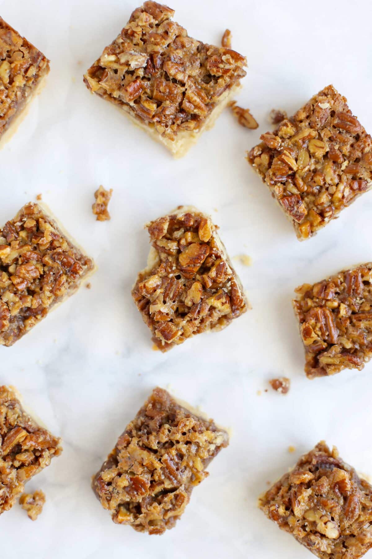 Pecan Pie Bars cut into squares and scattered on a sheet of white parchment paper.