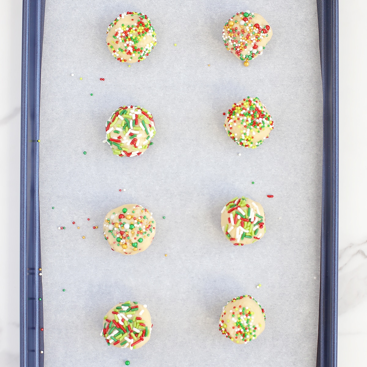 Balls of sugar cookie dough rolled in sprinkles on a baking sheet.
