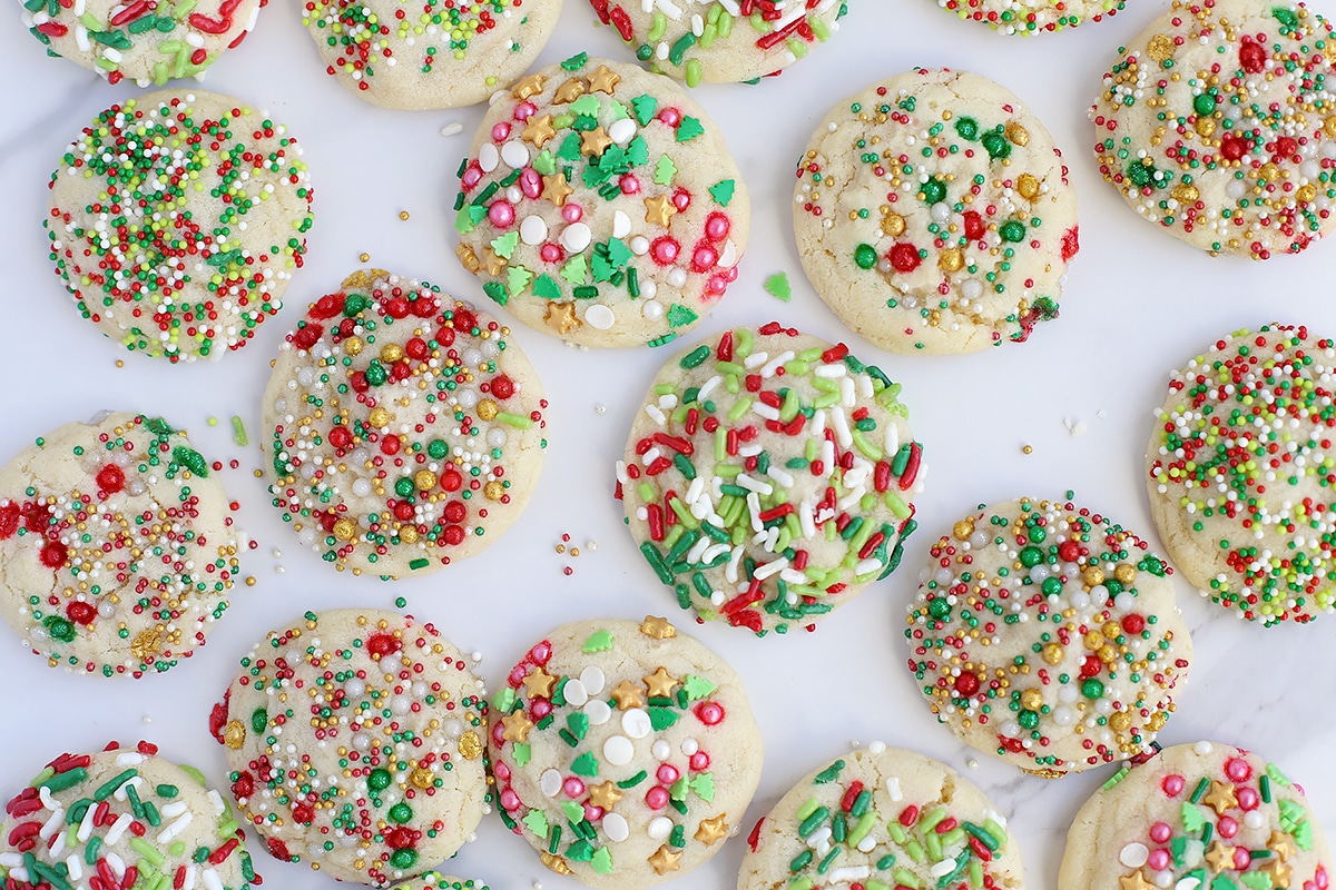 Holiday sugar cookies topped with colorful sprinkles spread out on a marble countertop.